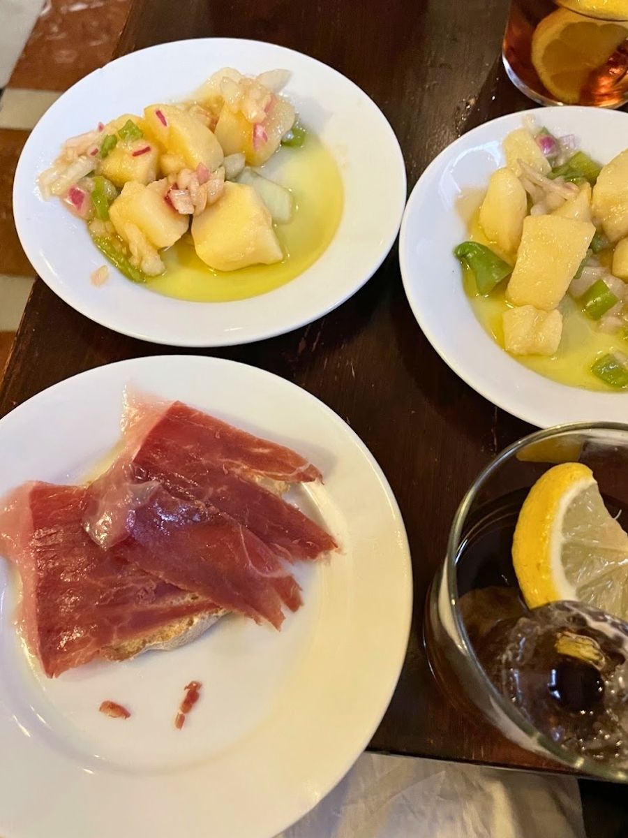 Plates of Spanish potato salad and jamón ibérico with a glass of vermouth during a Seville tapas tour